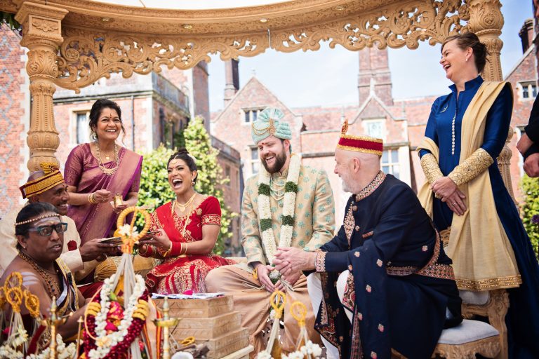 Bride and groom and family laugh during the Hindu ceremony at North Mymms Park, candidly photographed by Blooming Photography.