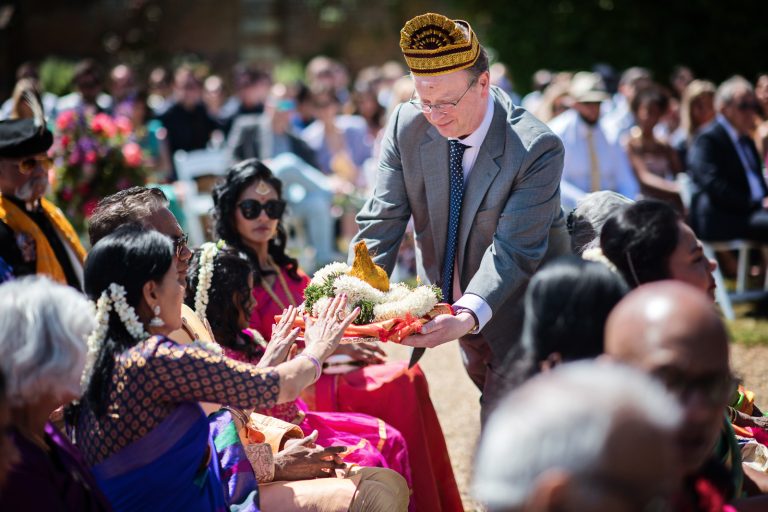 Wedding guest takes round wedding gifts to get them blessed during the Hindu ceremony at North Mymms Park, candidly photographed by Blooming Photography.i