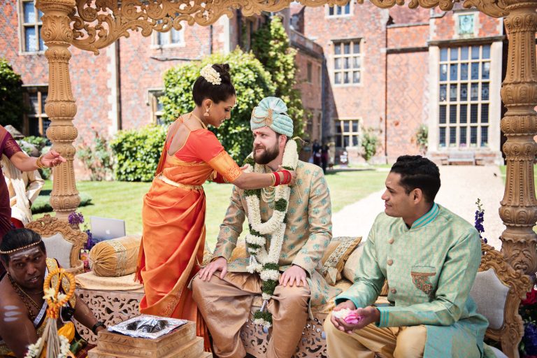 Bride gives her groom a flowered garland during Hindu ceremony at North Mymms Park, candidly photographed by Blooming Photography.