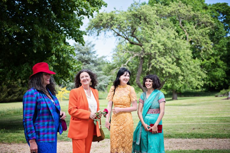 Colourful guests smile and chat in the grounds of North Mymms Park, candidly photographed by Blooming Photography.
