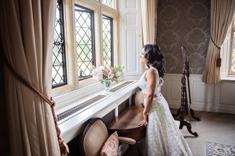 Glamorous photograph of a bride looking out of the huge elegant Georgian window Guests at North Mymms Park, candidly photographed by Blooming Photography.