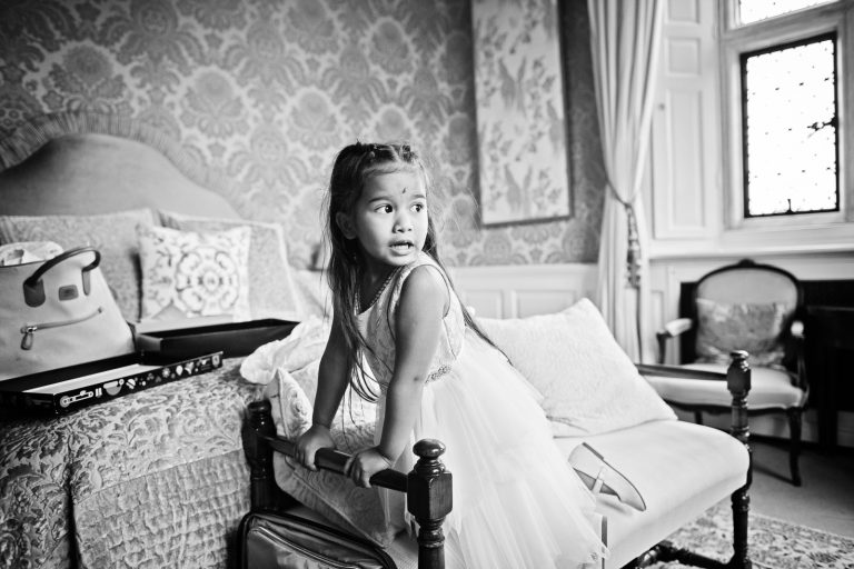 Black and white photo of a flowergirl playing on a chais longue at North Mymms Park, candidly photographed by Blooming Photography.