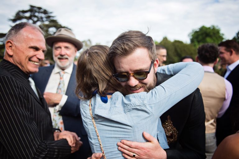 Candid, storytelling moment of an Auntie hugging the groom with family and guests around them. Photographed at North Mymms Park, by Blooming Photography.