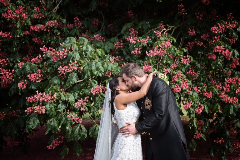 A bride and groom kiss with a horse chestnut tree in bloom. Photographed at North Mymms Park, by Blooming Photography.