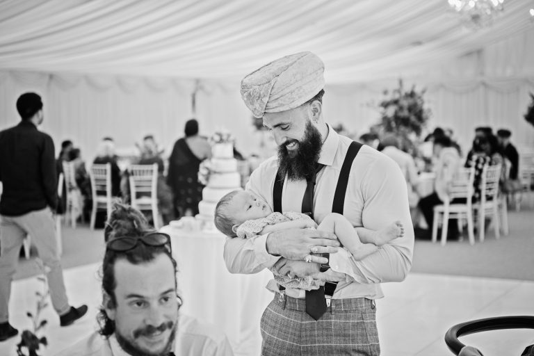 A groomsmen holds a baby, black and white photo. Photographed at North Mymms Park, by Blooming Photography.