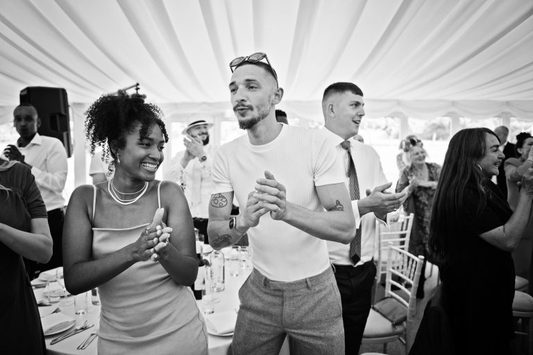 Guests cheer and clap as the bride and groom enter (not seen in pic). Black and white photo. Photographed at North Mymms Park, by Blooming Photography.