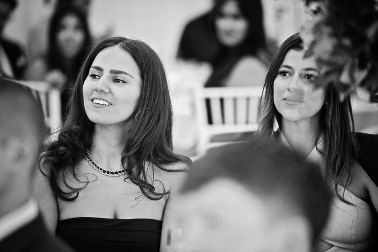 Wedding guest listens, smiling as they hear father of the bride speech. Photographed at North Mymms Park, by Blooming Photography.
