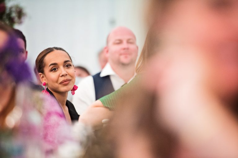A guest listens to speech. Lots of other people in photo but they are all out of focus. Photographed at North Mymms Park, by Blooming Photography.