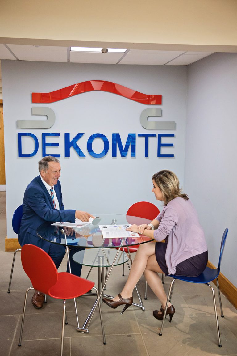 Portrait PR photograph of two colleagues sitting at a table looking at a company brochure with a Dekomte sign behind them.