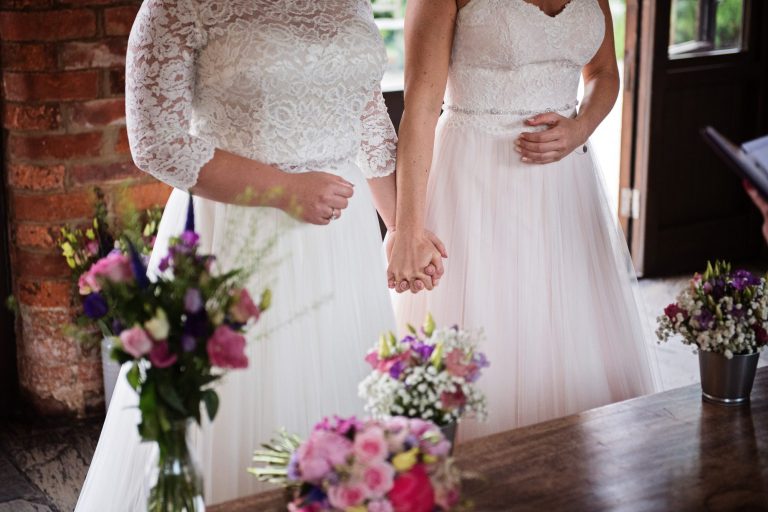 Bride and bride hold hands during wedding ceremony.