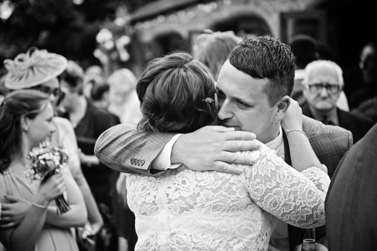 Candid b&w photograph of guests hugging the bride