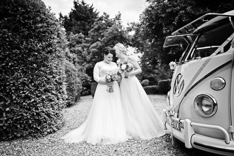 B&W storytelling image of bride and bride stood next to their VW campervan.