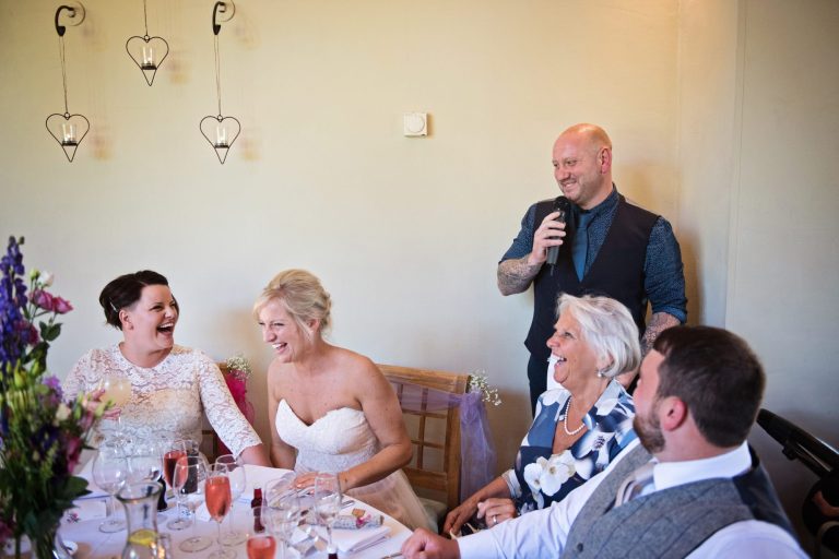 Bride and bride and guests laugh at the wedding speech.