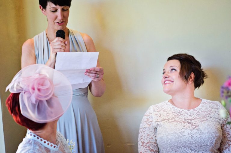 Storytelling photo of the brides sister delivering her speech. Bride is smiling.