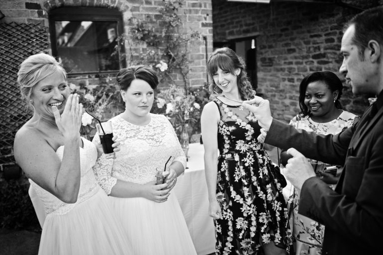 B&W documentary photo of bride and bride watching a magic trick in awe.