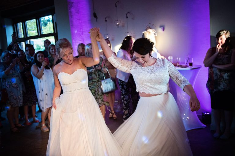 Bride and bride during their first dance with guests cheering and smiling surrounding them,