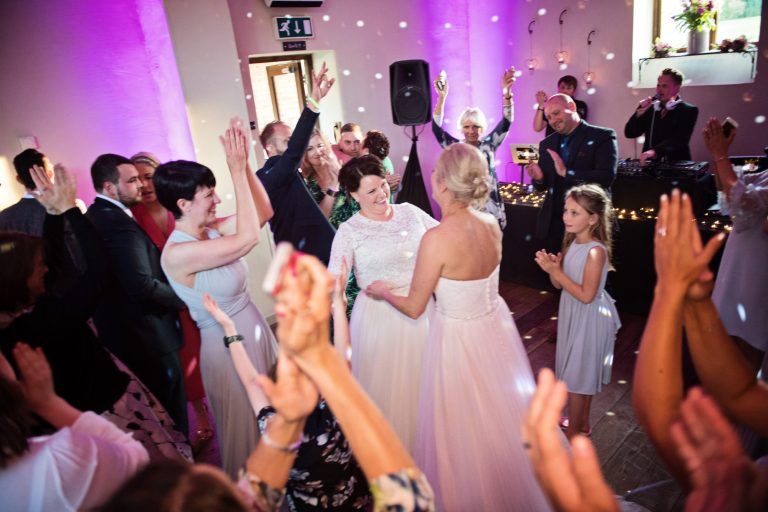 Bride and bride during their first dance with guests cheering and smiling surrounding them,