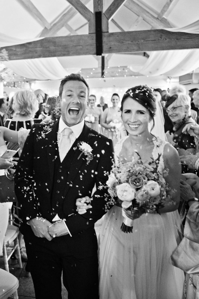 B&W fun photo of bride and groom exiting the West Sussex wedding venue.