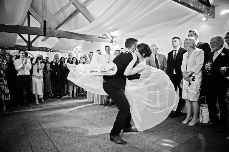 B&W fun photo of first dance at a wedding where the groom is spinning his wife on the dance floor.