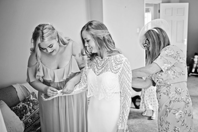 Bridesmaid and mother of the bride help fit the brides dress. B&W candid photo.
