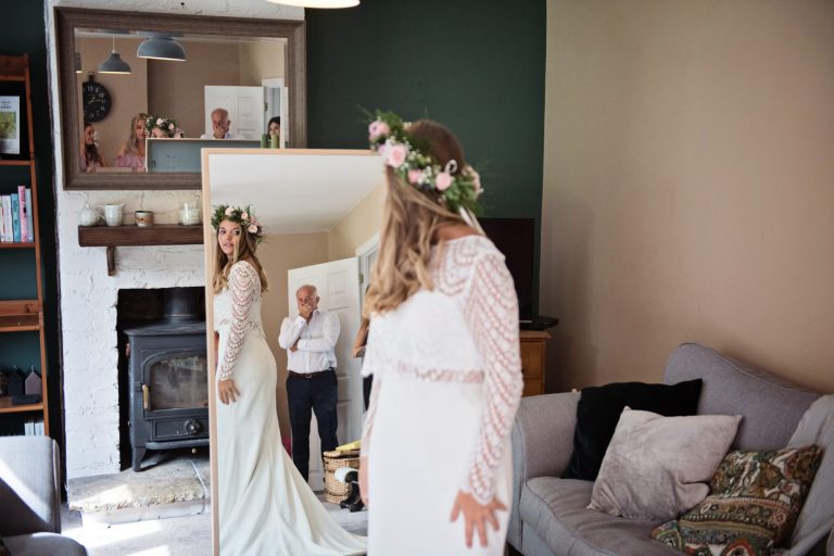 Candid photo of bride looking in the mirror at her dress. You can see dad blown away with emotion in the relfection.