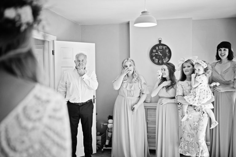 B&W photo of Dad, mum and bridesmaids, cry with happy emotion after seeing the bride in her wedding dress for the first time.