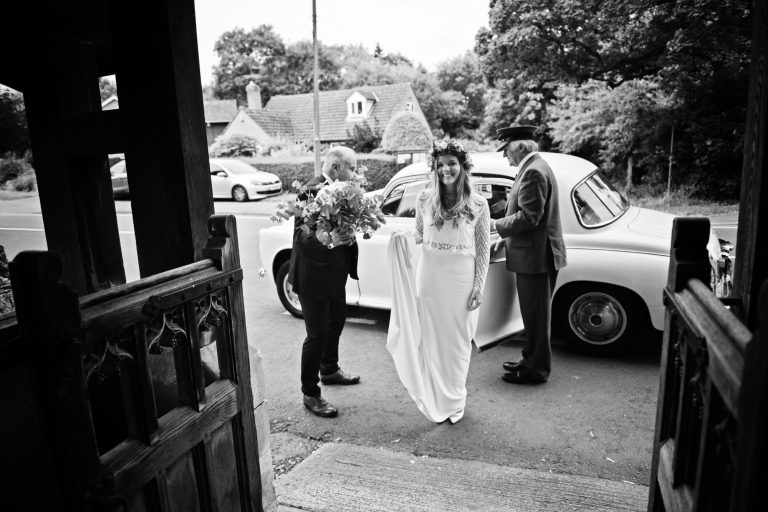 B&W timeless candid photo of bride getting out of her wedding car, with her dad next to her.