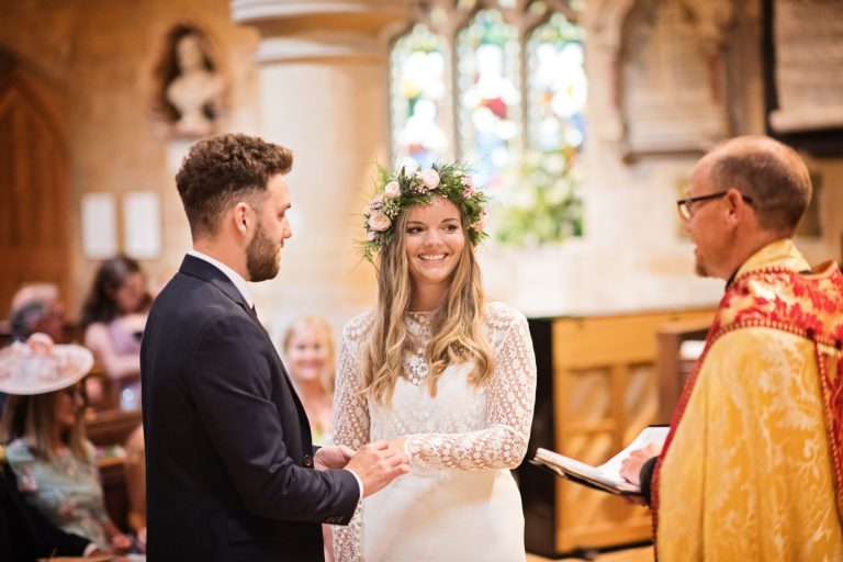 Colour candid pic of bride and groom smiling as they say their wedding vows to the vicar in the church.