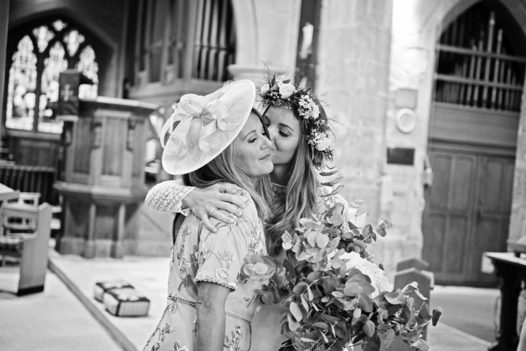 B&W candid photo of bride hugging and kissing her mum.