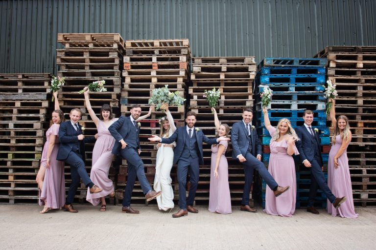 Fabulous photo of bride and groom and bridal party having fun and posing in front of wooden pallets for their wedding at Overbarn, Gloucester.