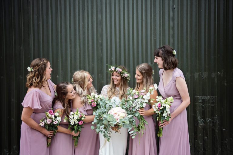 Bride and bridesmaids pose with their wedding flower bouquets pose in front of an agricultural building.