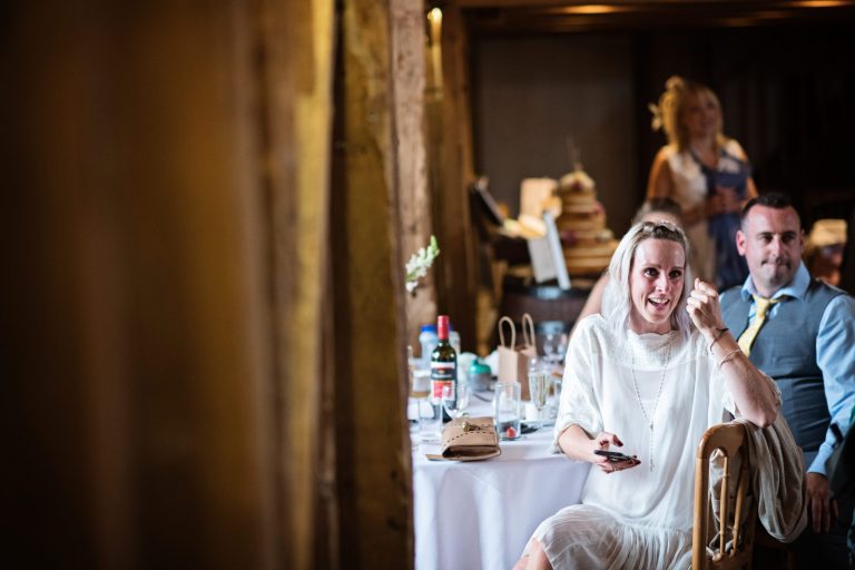 Documentary style photo of a wedding guest smiling a listening to the wedding speech.