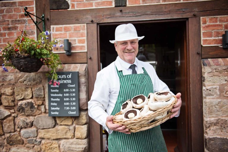 Headshot of a butcher carrying a basket of veg.