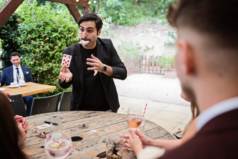 A magician entertaining wedding guests with half the playing cards in his mouth, and playing card in his right hand (the 7 of hearts).