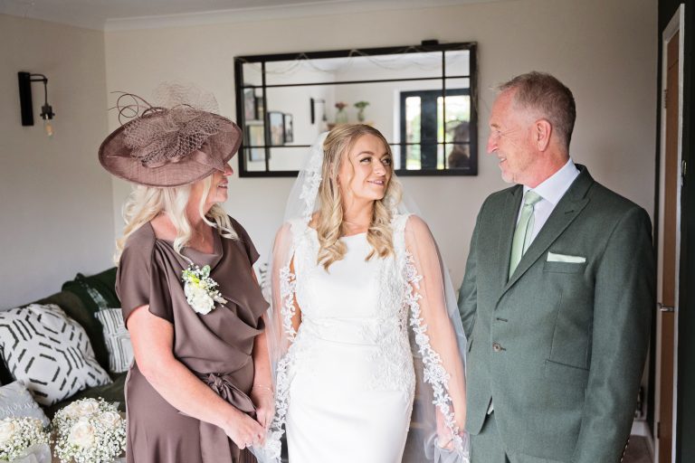 mother of the bride, bride and father of the bride smiling and holding hands