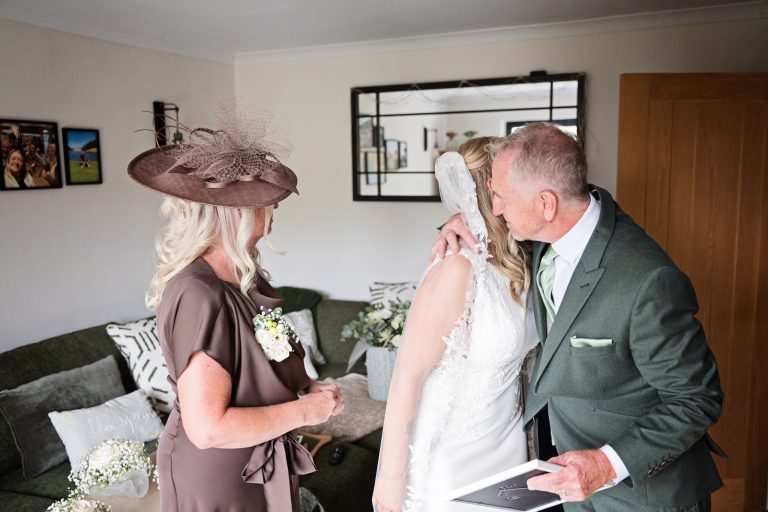bride and father of the bride hugging with the mother of the bride watching