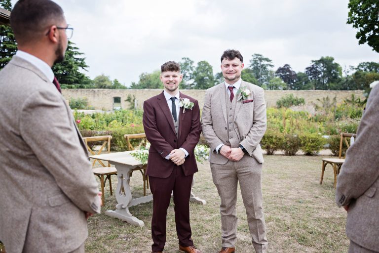groom and best man stand facing the camera with the groomsmen standing either side facing them