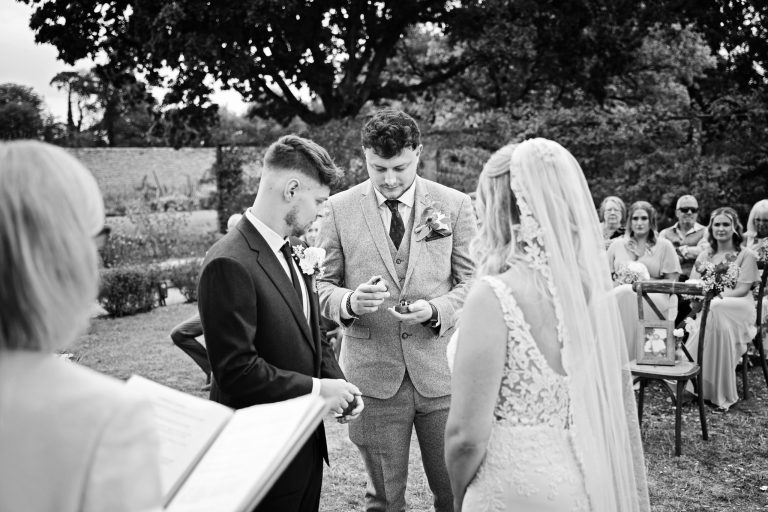 B & w image of the best man giving the groom the wedding rings
