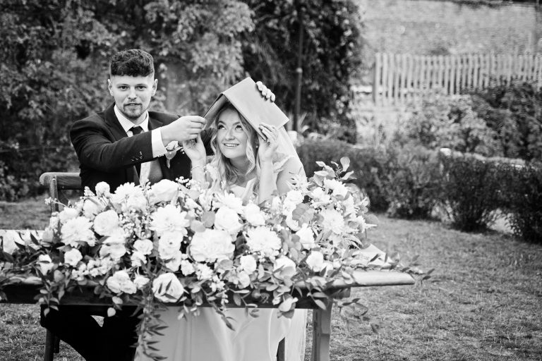 B&w image of a groom holding the register over the brides head as it's just started to rain!