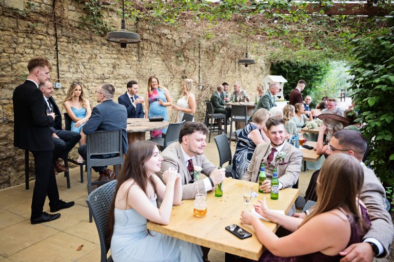 Wedding guests sit and chat around tables under a green canopy