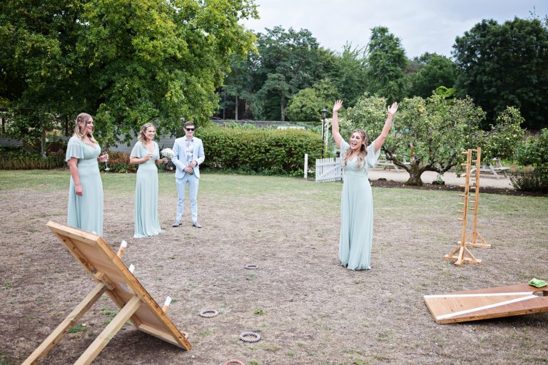 a bridesmaid with her hands in the air as she celebrates winning a garden game. Bridesmaids smiling at her.