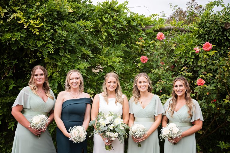 Bridesmaids stand smiling holding their wedding flowers in the Gardens of Old Down Barn