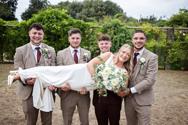 fun image of groomsmen and groom carrying his bride who is holding the wedding bouquet