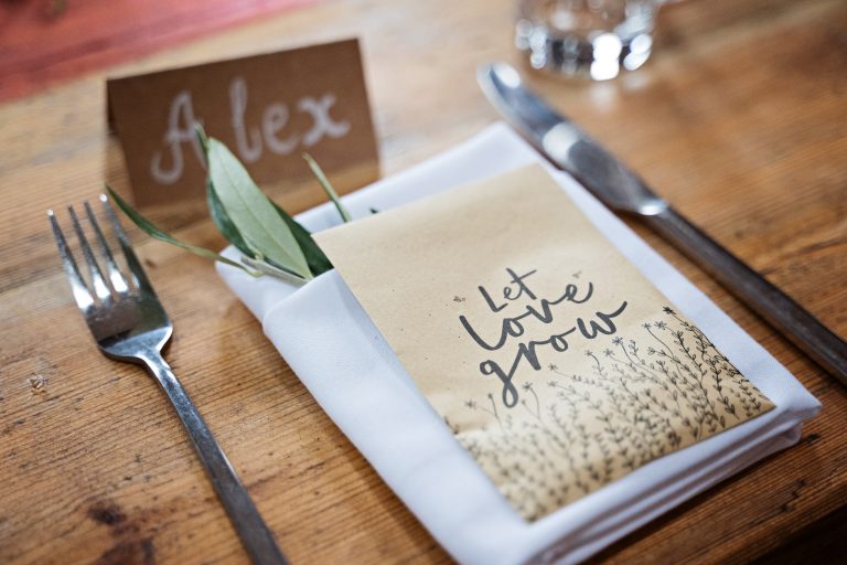 Wedding breakfast table set up, knife, fork plus napkins, bayleaf and a seed packet with "Let Love Grow" written on it.