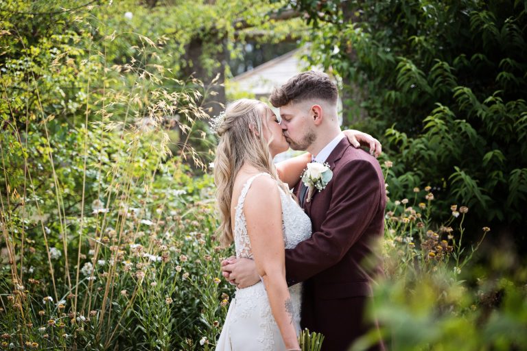 image of bride and groom kissing each other as they are in a cottage garden.