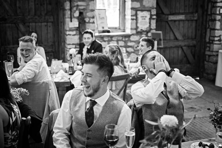 B &W image of guests laughing at one of the jokes inn a wedding speech.