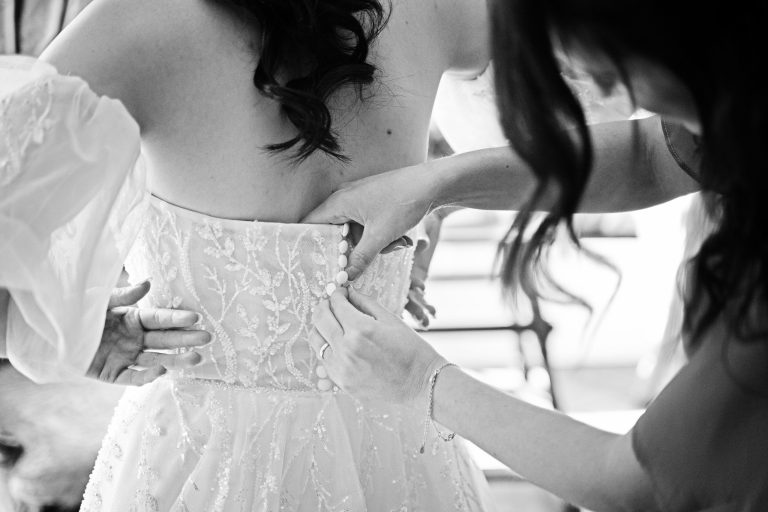 A B&W close up image of the back of a bride who is getting in her wedding dress