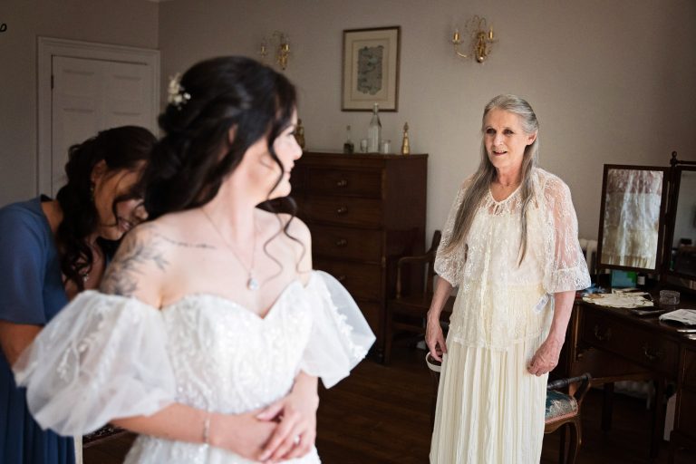 A brides mum watches as her daughter is getting in her wedding dress.
