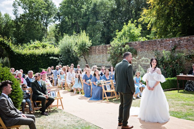 A bride and groom say their wedding vows . Wedding guests smiling in the background