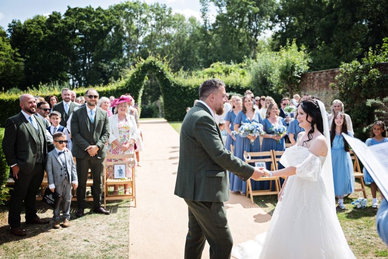 A bride and groom say their wedding vows . Wedding guests smiling in the background